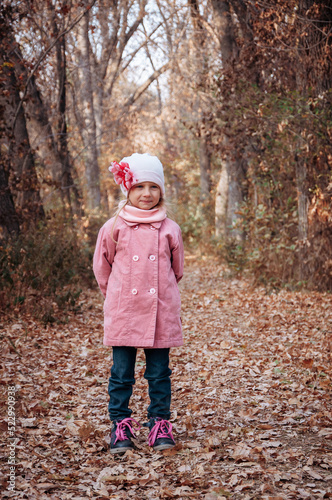 A cheerful girl in a pink coat stands in an autumn park