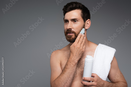 bearded man with towel applying shaving foam isolated on grey. photo