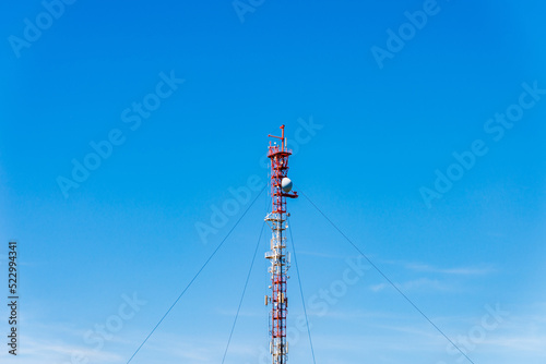 Cell tower, cellular antenna against the blue sky. Copy space.Tower poles and wireless telephone antenna is red.