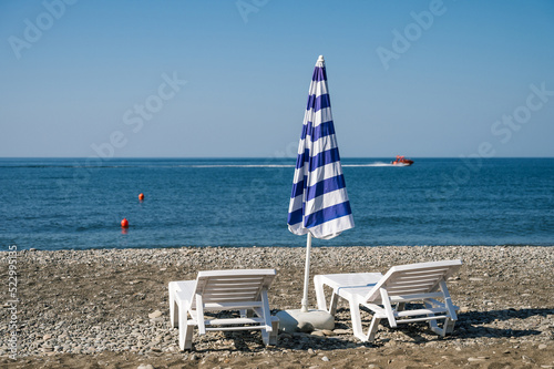 Two sun loungers and a beach umbrella by the sea on a pebble beach. Summer vacation.