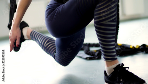close-up, female legs in leggings and sneakers. woman performs exercises on TRX loops, Straps, goes in for sports,