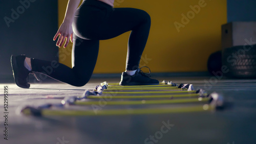 close-up, female legs in black leggings and sneakers. woman performs exercises with an athlete's foot ladder, jumps , training on agility ladder on floor, in gym. Fitness class cardio workout