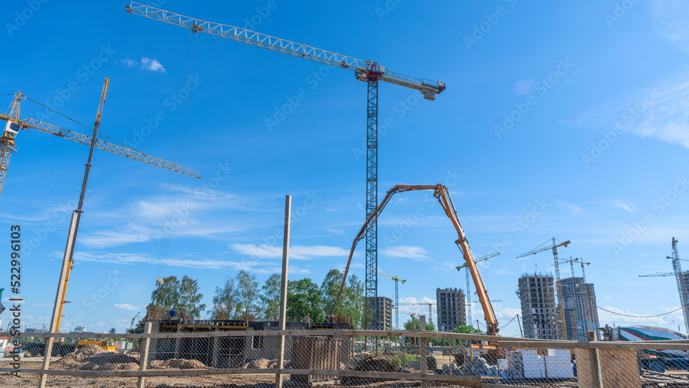 Construction of a multi-story residential buildings. Defocused foreground with young tree. Cranes work. Construction site.