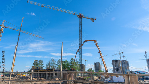 Construction of a multi-story residential buildings. Defocused foreground with young tree. Cranes work. Construction site.