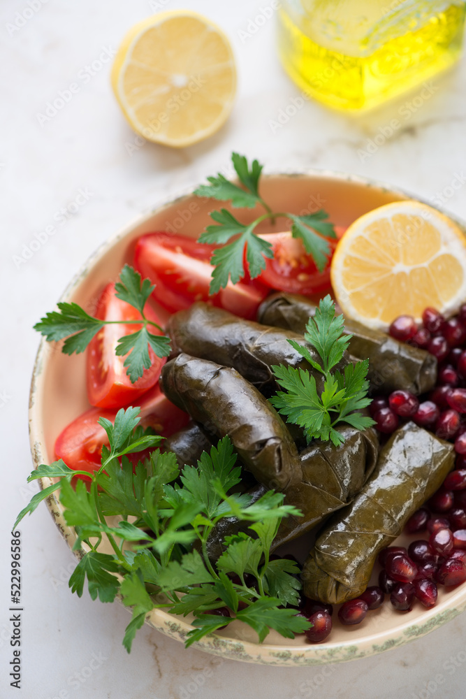 Dolma or stuffed grape leaves served with pomegranate seeds, tomatoes, lemon and fresh parsley, middle closeup, vertical shot Dolma or stuffed grape leaves served with pomegranate seeds, tomatoes, lemon and fresh parsley, middle closeup, vertical shot