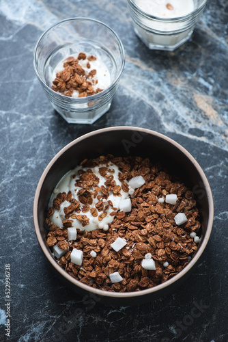 Bowl of chocolate granola with coconut and greek yogurt, vertical shot on a black marble background