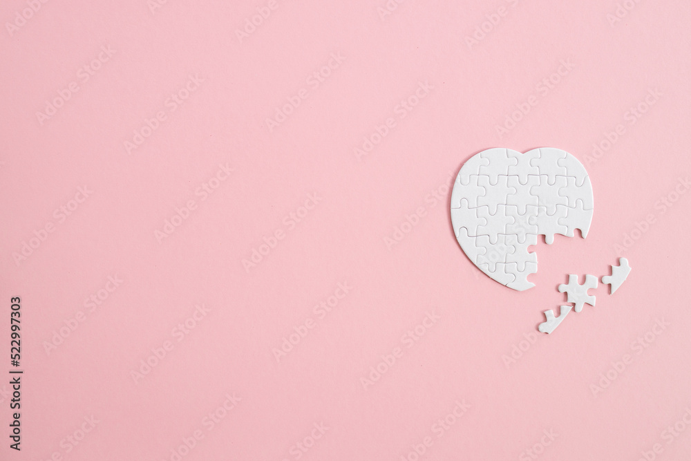 Top view white heart puzzle with a missing piece over pink background.
