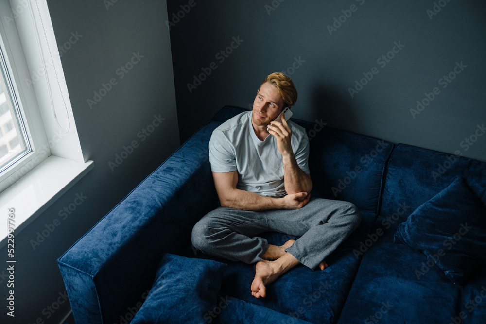 Young bearded man using cellphone while sitting on sofa at home Young bearded man using cellphone while sitting on sofa at home