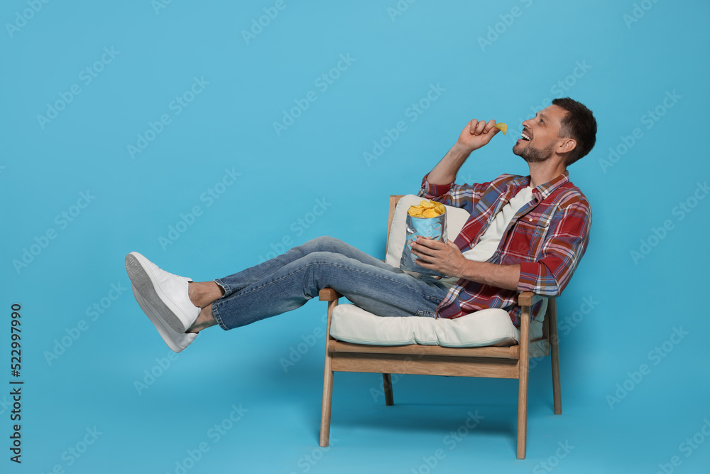 Handsome man eating potato chips on light blue background