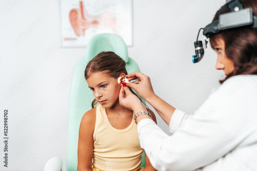 Female audiologist examining girl ear using otoscope in doctors office