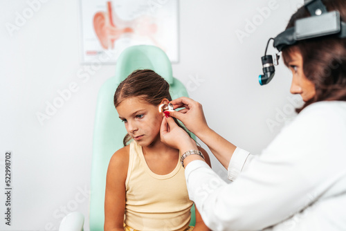 Female audiologist examining girl ear using otoscope in doctors office. Child receiving a ear exam. Nose and throat medical examination. Healthcare and medicine concept. photo