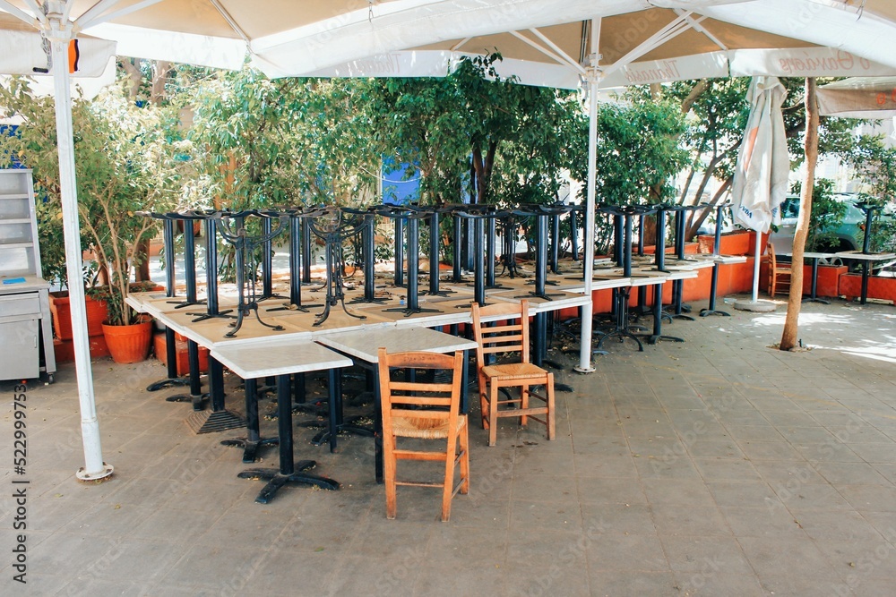 Fototapeta premium Tables and chairs stacked outside closed cafe-restaurant during the Coronavirus lockdown - Athens, Greece, May 6 2020.