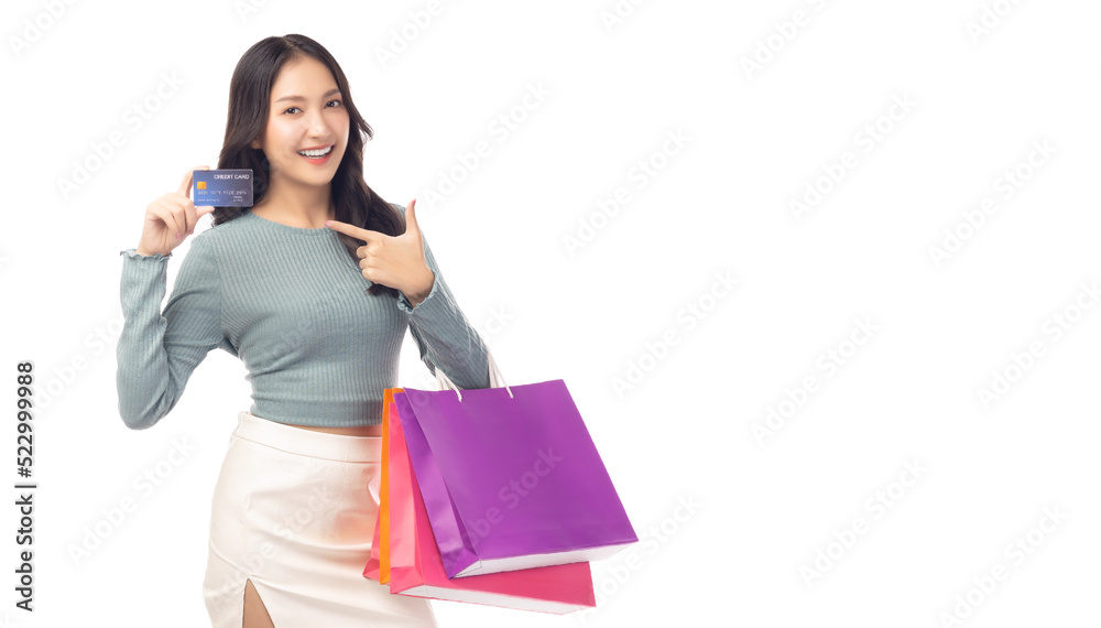 Trendy young Asian woman hold plastic credit card and shopping bags pointing up to credit card Beautiful shopping girl point to credit card with smile Looking at camera Isolated on white background