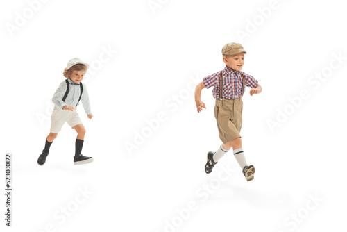 Two preschool age boys, stylish kids wearing retro clothes running isolated over white background. Concept of childhood, vintage summer fashion style