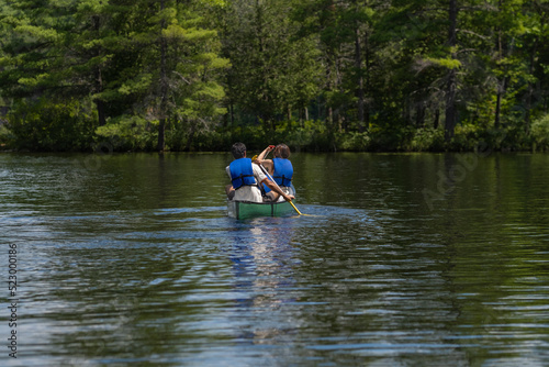 Couple in life vests paddling in a kayak on a lake surrounded by thick coniferous forest, sunny summer day, selective focus. Water sports, recreation, adventure concept.