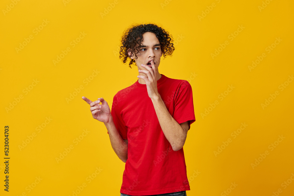 Shocked funny Caucasian young man in red t-shirt point finger aside posing isolated on over yellow studio background. The best offer with free place for advertising. Emotions for everyday concept