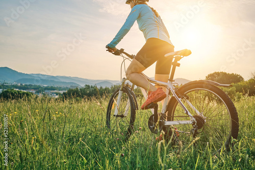 Fototapeta Naklejka Na Ścianę i Meble -  Cyclist Woman riding bike in helmets go in sports outdoors on sunny day a mountain in the forest. Silhouette female at sunset. Fresh air. Health care, authenticity, sense of balance and calmness.	
