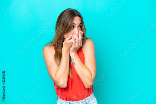 Young caucasian woman isolated on blue background covering mouth and looking to the side