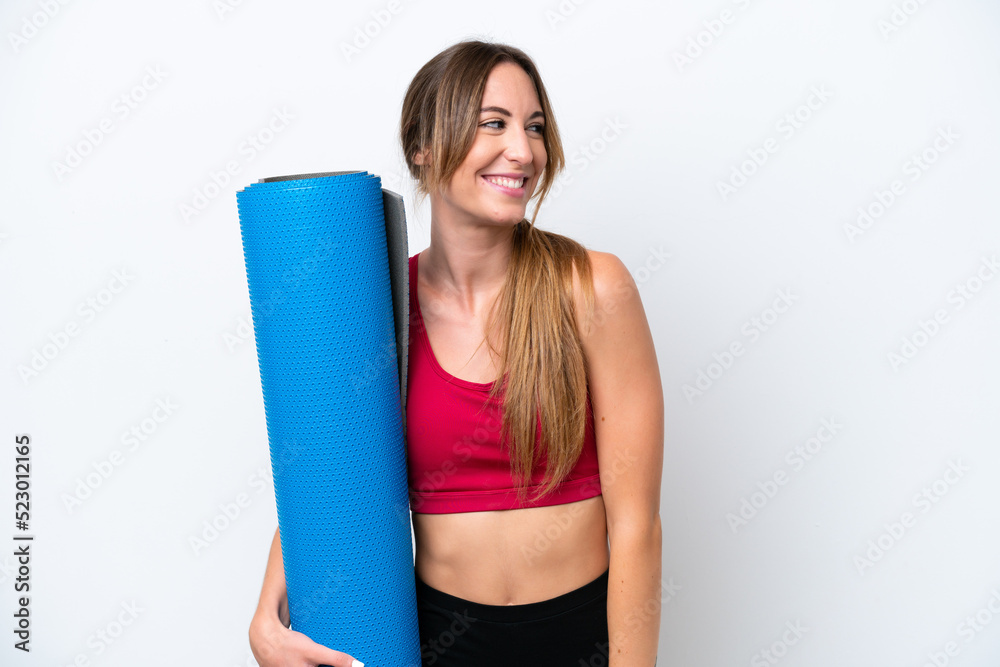 Young sport woman going to yoga classes while holding a mat isolated on white background looking to the side and smiling