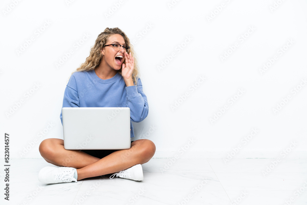 Girl with curly hair with a laptop sitting on the floor shouting with mouth wide open to the lateral