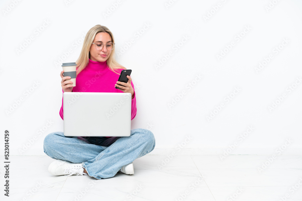 Young caucasian woman with laptop sitting on the floor holding coffee to take away and a mobile Young caucasian woman with laptop sitting on the floor holding coffee to take away and a mobile