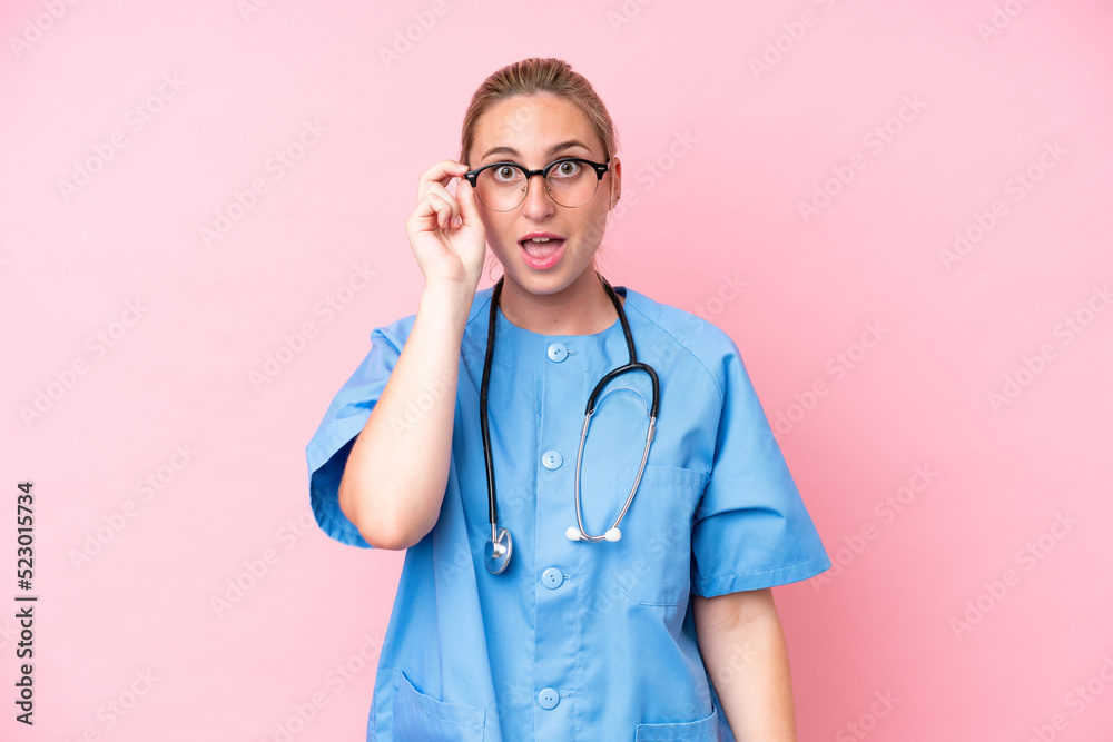Young surgeon nurse woman isolated on pink background with glasses and surprised Young surgeon nurse woman isolated on pink background with glasses and surprised