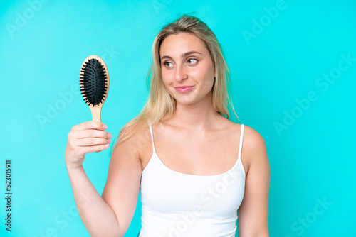 Young caucasian woman with hair comb isolated on blue background with happy expression