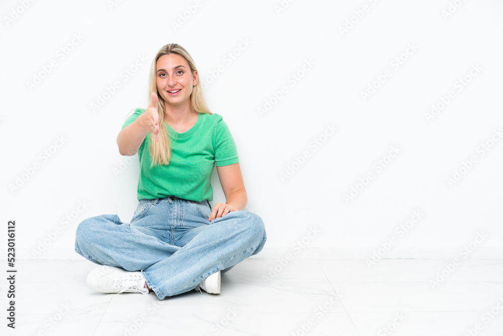 Young caucasian woman sitting on the floor isolated on white background shaking hands for closing a good deal Young caucasian woman sitting on the floor isolated on white background shaking hands for closing a good deal
