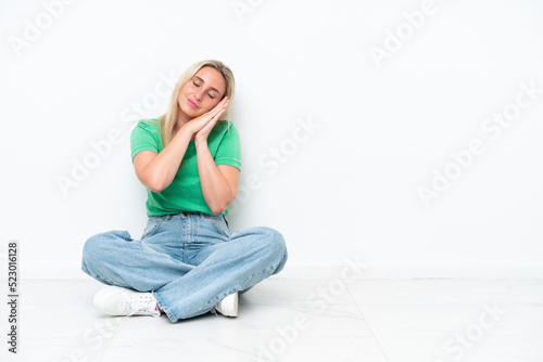 Young caucasian woman sitting on the floor isolated on white background making sleep gesture in dorable expression
