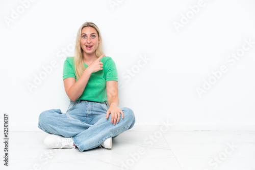 Young caucasian woman sitting on the floor isolated on white background surprised and pointing side