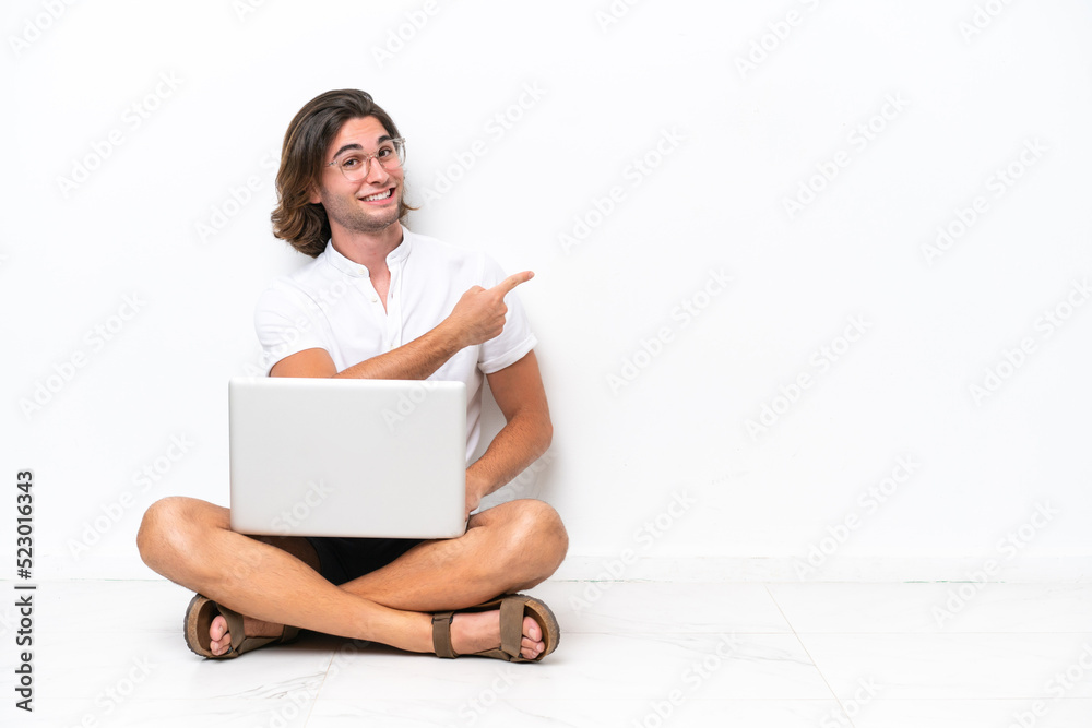 Young handsome man with a laptop sitting on the floor isolated on white background pointing back Young handsome man with a laptop sitting on the floor isolated on white background pointing back