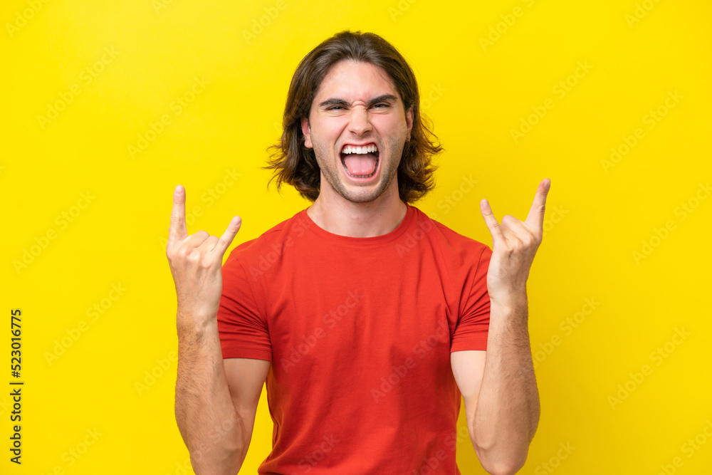 Caucasian handsome man isolated on yellow background making horn gesture Caucasian handsome man isolated on yellow background making horn gesture