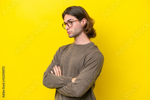 Caucasian handsome man isolated on yellow background keeping the arms crossed