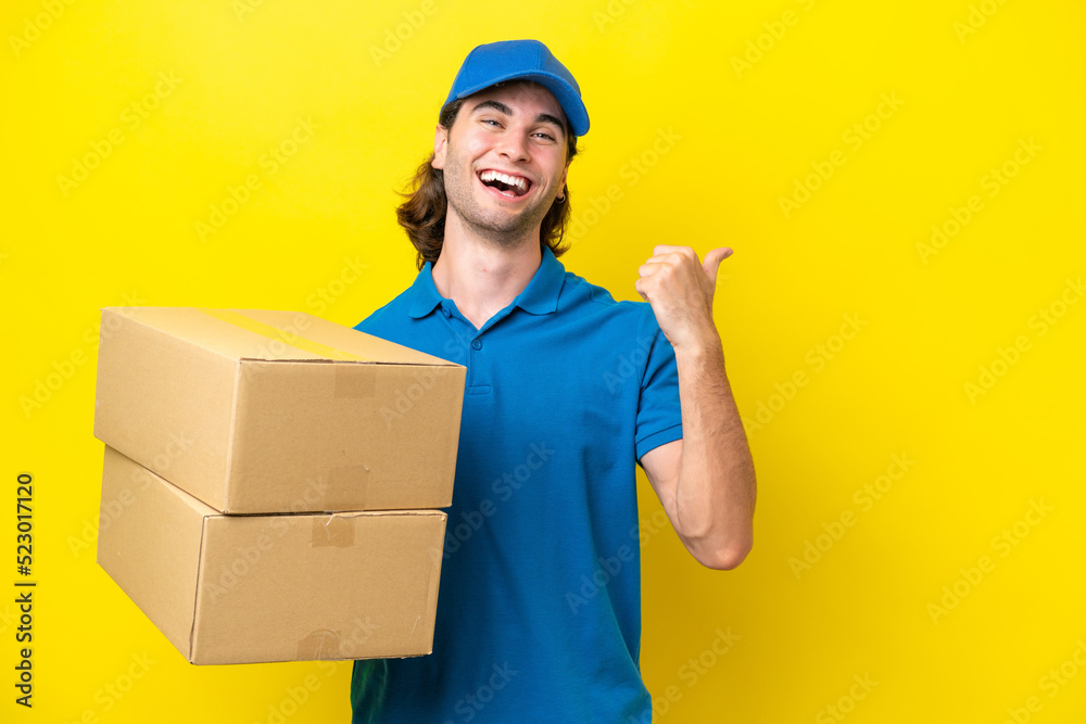 Delivery handsome man isolated on yellow background pointing to the side to present a product Delivery handsome man isolated on yellow background pointing to the side to present a product