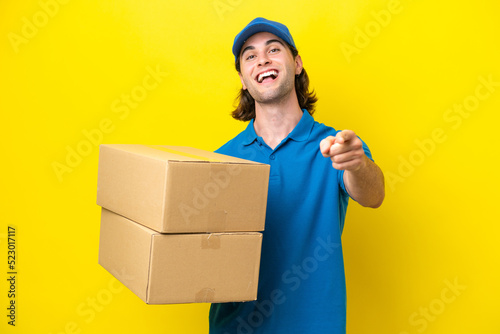 Delivery handsome man isolated on yellow background surprised and pointing front