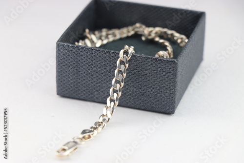 Silver chain with details of chain links out of the box that is worn as a necklace or fashion jewelry kept in a box on white background