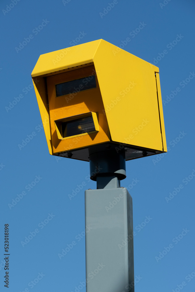 Low angle view of bright yellow speed safety camera against a clear blue sky background. Low angle view of bright yellow speed safety camera against a clear blue sky background.