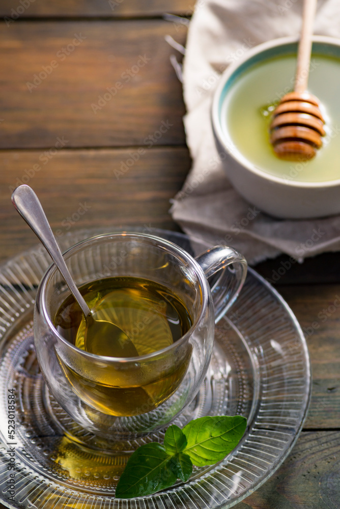 Herbal mint tea cup Transparent glass dark background wooden table still life honey bowl metal kettle teapot spoon cozy