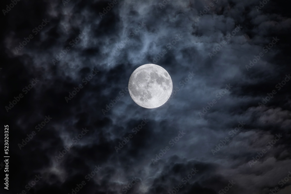 Full moon at night. The illuminated face of the moon is wrapped in a cloud cover that covers it in a veiled way. Full moon at night. The illuminated face of the moon is wrapped in a cloud cover that covers it in a veiled way.