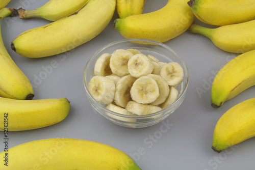 Whole and sliced bananas in bowl on gray background. 