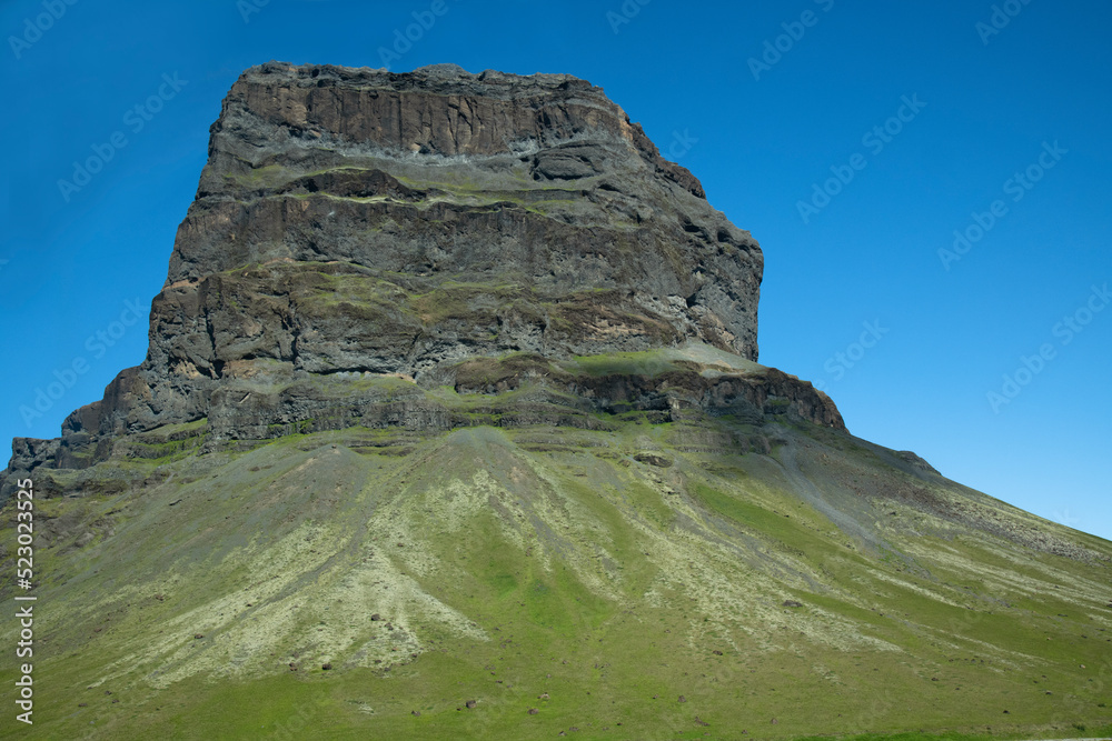 großer massiver Felsen auf einem grünen Berg vor blauem Himmel