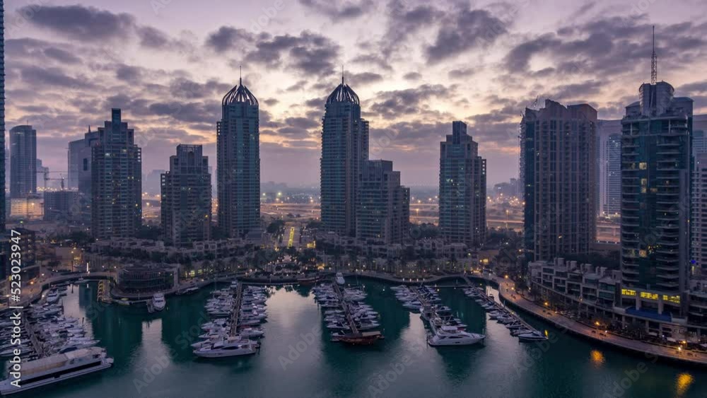 Aerial panoramic view of modern skyscrapers night to day transition timelapse before sunrise in Dubai Marina with yachts in Dubai, UAE. Illuminated towers early morning Aerial panoramic view of modern skyscrapers night to day transition timelapse before sunrise in Dubai Marina with yachts in Dubai, UAE. Illuminated towers early morning