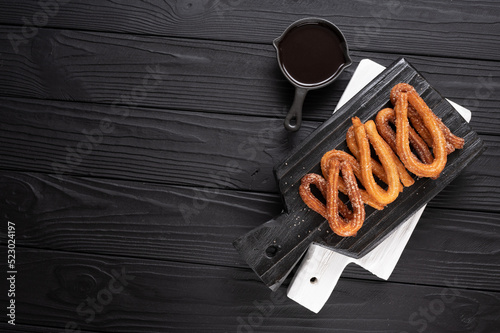 Homemade churros with chocolate on a dark wooden rustic background.
