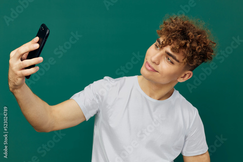a handsome, joyful man takes a selfie on his phone, smiling pleasantly, standing on a green background