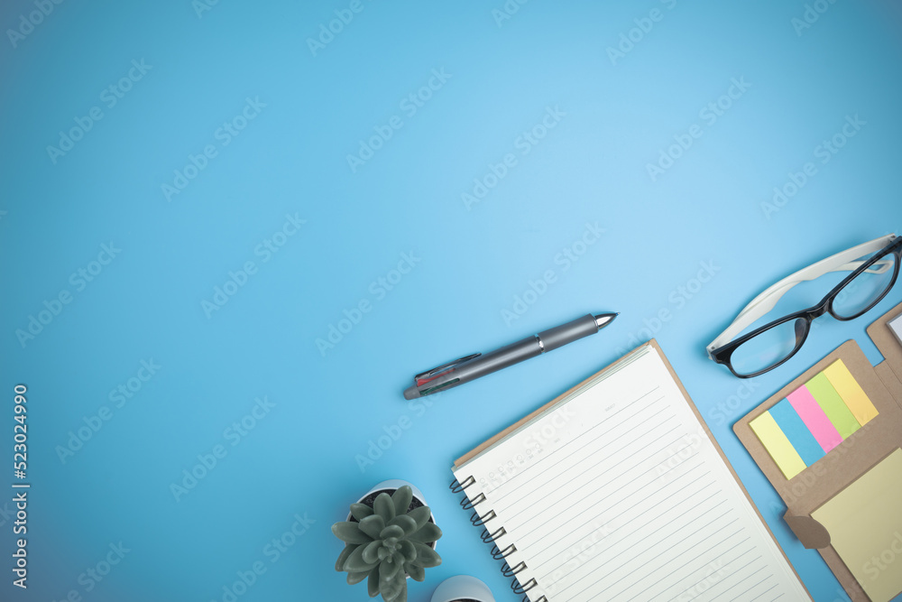 Office table desk of the business flat lay, background. Top view workspace of table office with copy space. Business concept. The blue office desk with a notebook, a pen, glasses, and a mini tree. Office table desk of the business flat lay, background. Top view workspace of table office with copy space. Business concept. The blue office desk with a notebook, a pen, glasses, and a mini tree.