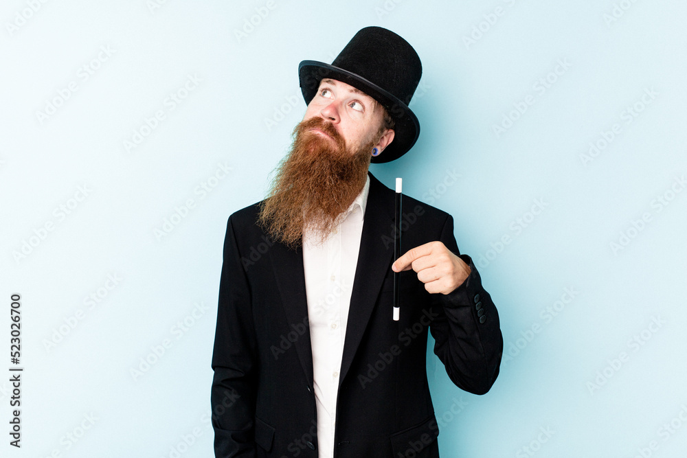 Young magician man isolated on blue background dreaming of achieving goals and purposes Young magician man isolated on blue background dreaming of achieving goals and purposes