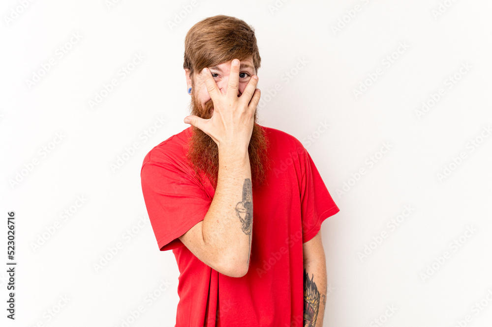 Young caucasian red-haired man isolated on white background blink at the camera through fingers, embarrassed covering face. Young caucasian red-haired man isolated on white background blink at the camera through fingers, embarrassed covering face.