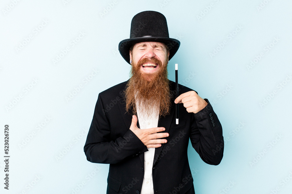Young magician man isolated on blue background laughs out loudly keeping hand on chest. Young magician man isolated on blue background laughs out loudly keeping hand on chest.