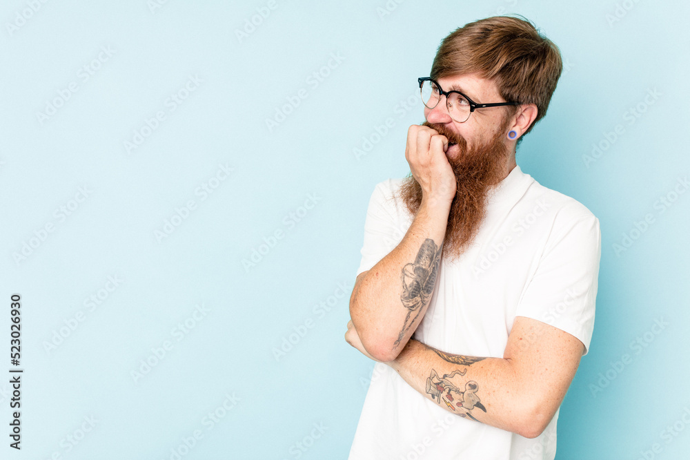 Young caucasian red-haired man isolated on blue background relaxed thinking about something looking at a copy space. Young caucasian red-haired man isolated on blue background relaxed thinking about something looking at a copy space.