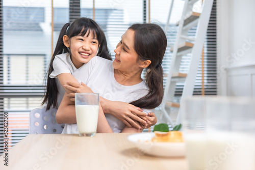 Asian  family enjoying breakfast at living room. little girl daughter sitting on table  drinking milk with smiling father and mother in morning. Happy family at home.